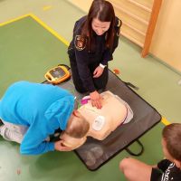 Funkcjonariuszka uczy chłopca uciskania klatki piersiowej na fantomie